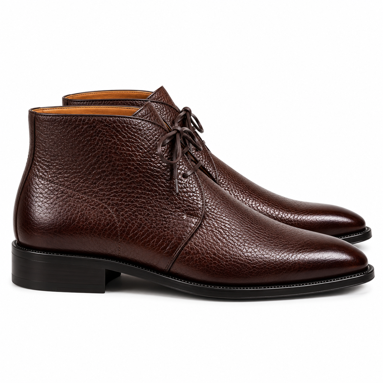 Front view of a pair of dark chocolate-brown genuine leather chukka-style ankle boots featuring pebbled grain-textured uppers, dark brown laces, polished pointed almond-shaped toes, tan-colored interiors, and black sole edges against a white background.