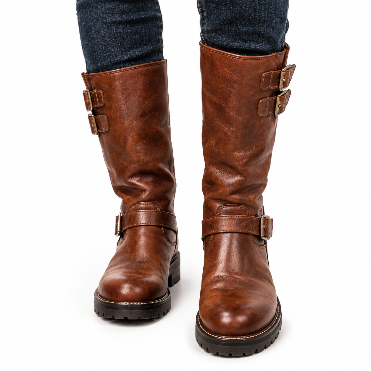 Three-quarter side view of one pair of Mizon International vintage cognac-brown biker boots with genuine leather uppers, tall shafts, antique brass-tone buckle straps, rounded toes, contrasting tan stitching, and thick black lug-pattern soles against a white background.